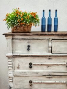 Stylish rustic dresser with blue bottles and a vibrant flower basket, perfect for decor inspiration.