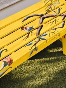 Vibrant wooden bench with bird and branch art in a sunny setting.
