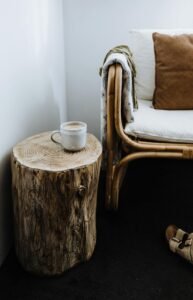 Interior of room with hot latte in ceramic mug placed on stump near chair with soft pillows