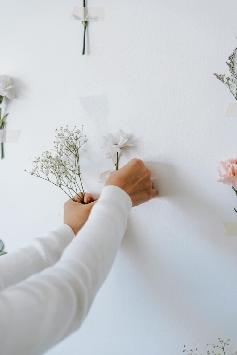 Crop unrecognizable decorator gluing delicate gypsophila and carnation to white wall making composition